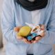 Senior gray bearded excited man in scarf having acute viral infection holding many anti-inflammatory drugs in hands in living room at home