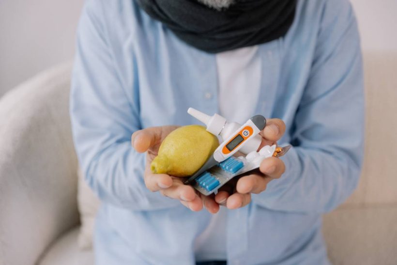 Senior gray bearded excited man in scarf having acute viral infection holding many anti-inflammatory drugs in hands in living room at home