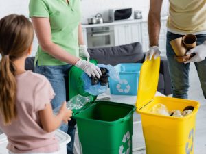 Parents in latex gloves sorting garbage near blurred daughter with bottle at home