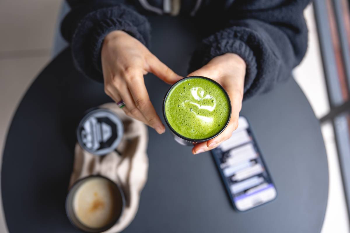 A woman holding in hands trendy green matcha drink and smartphone, top view.