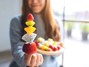 Closeup image of an asian woman holding and showing a fresh mixed fruits on skewers