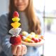 Closeup image of an asian woman holding and showing a fresh mixed fruits on skewers