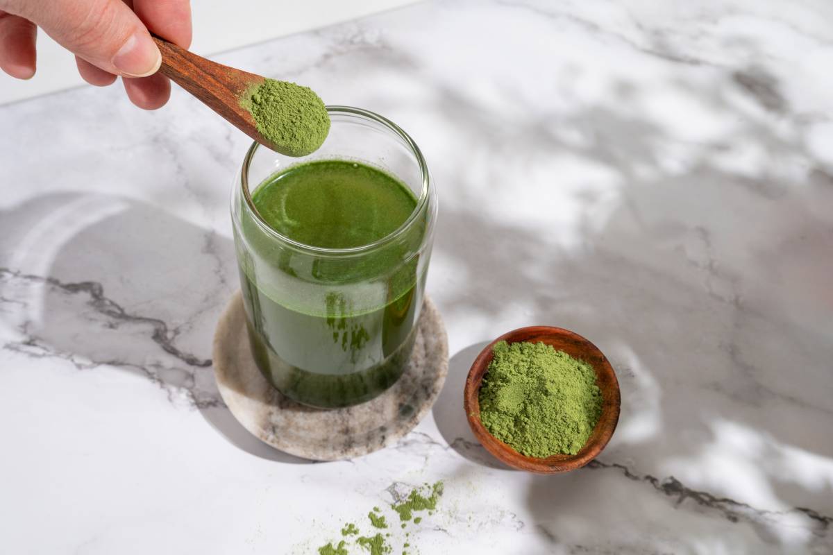 Hand pouring powder of young barley and chlorella spirulina or matcha into a glass.