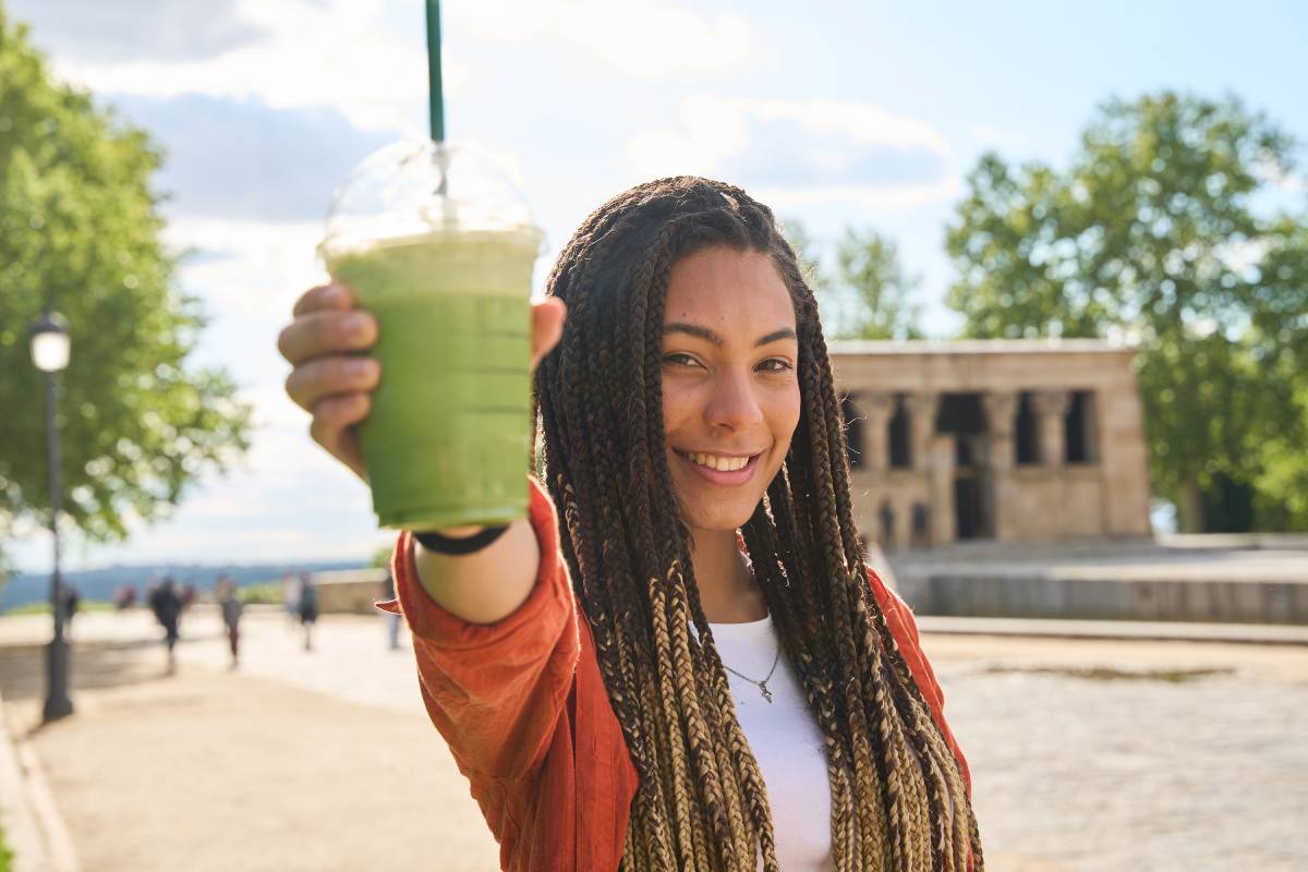 Young latin woman showing a green smoothie in debod temple, madrid