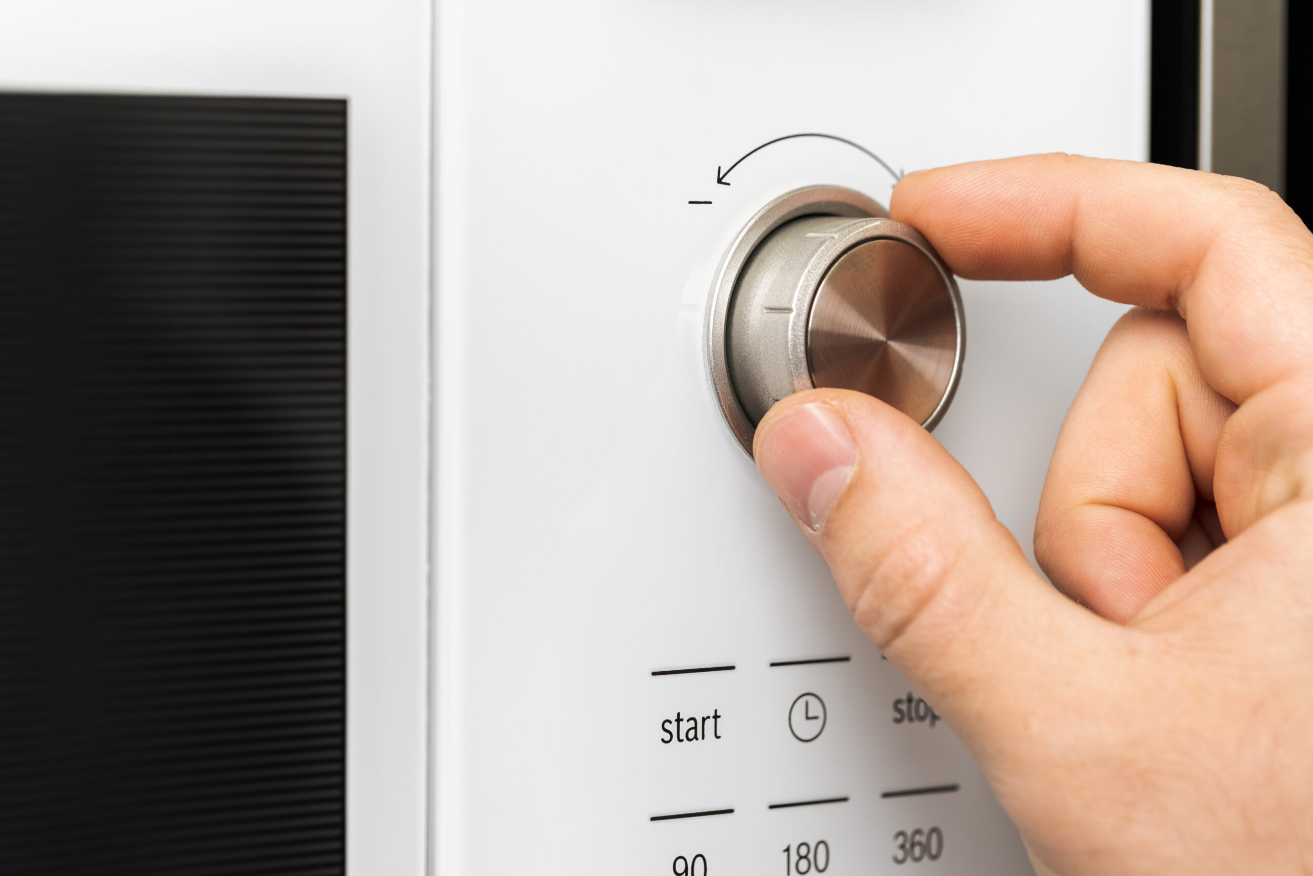 Hand pushing button of microwave oven for cooking food in kitchen
