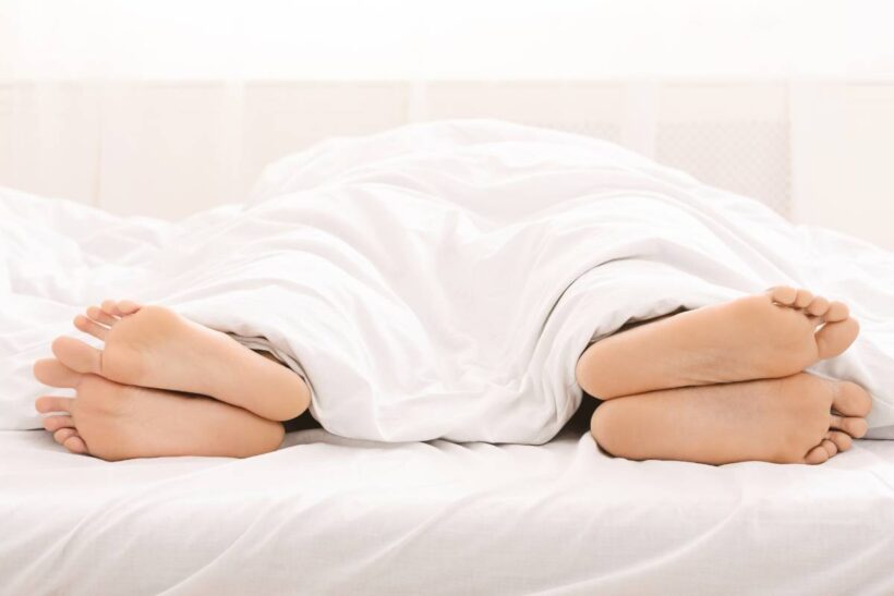 Relationship crisis. Bare feet of couple sleeping separately in bed, free space