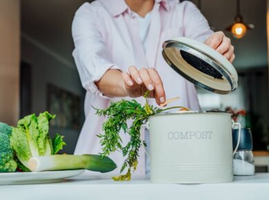 Compost the kitchen waste, recycling at home. Woman putting vegetables cutted leftovers into the garbage, compost bin on the table of her kitchen.